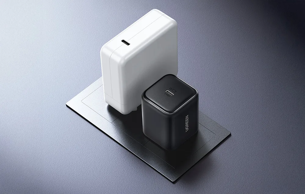 Compact UGREEN X524 black charger compared with a larger white charger to show size difference