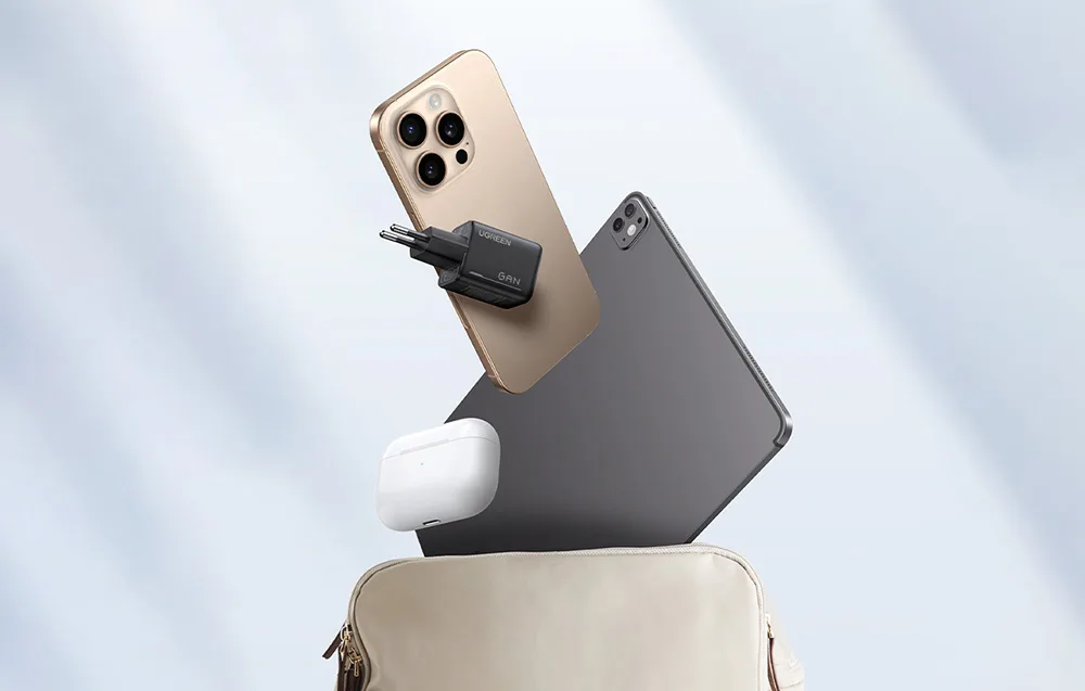 UGREEN GaN charger next to a smartphone, tablet, and earbud case floating above an open bag