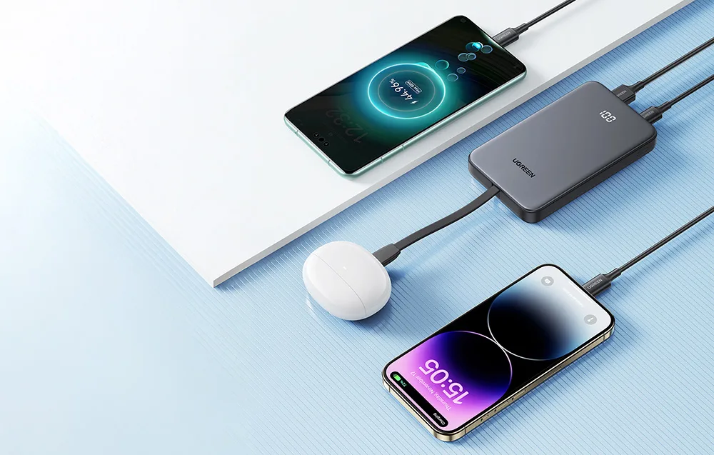 Powerbank Ugreen ładujący jednocześnie trzy urządzenia: dwa smartfony i etui ze słuchawkami bezprzewodowymi.