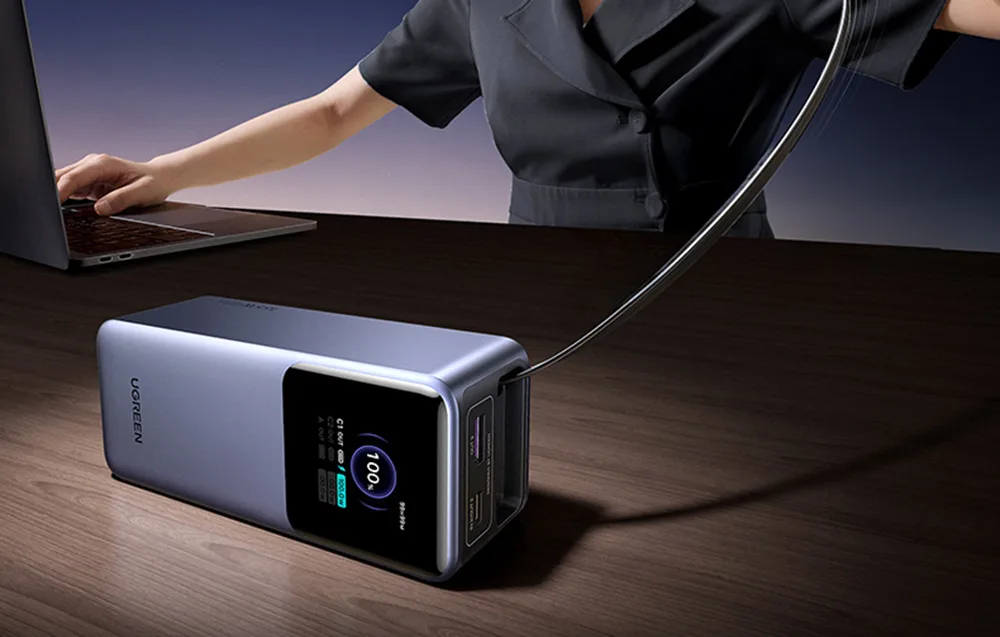 Ugreen PB726 power bank charging near a laptop on a dark desk
