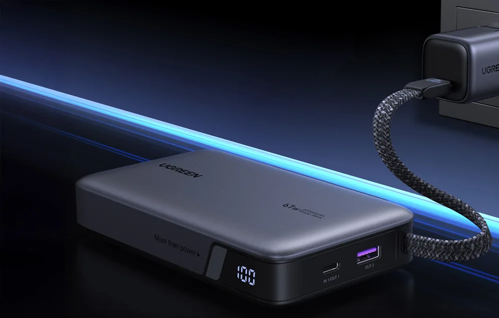 Ugreen PB550 power bank connected to a wall charger with digital battery display showing 100 percent and visible USB-C and USB-A ports.