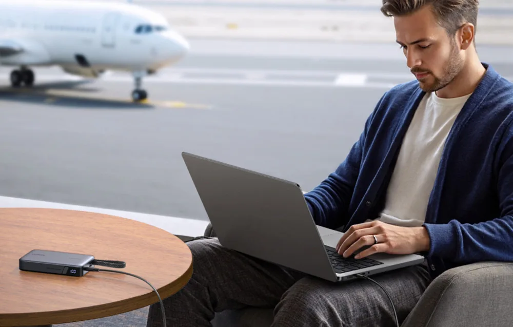 Man working on a laptop at an airport terminal while charging it with the Ugreen PB550 power bank.