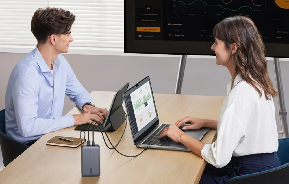 Ugreen PB550 power bank charging a laptop and tablet during a desk meeting.