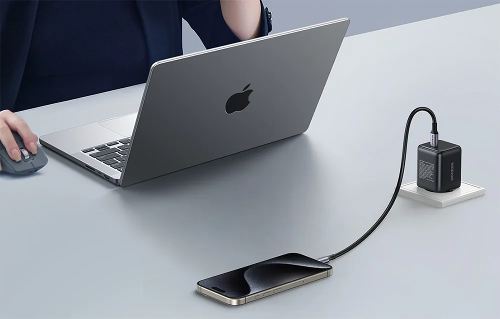 UGREEN X513 black charger charging a smartphone next to an open laptop on a desk