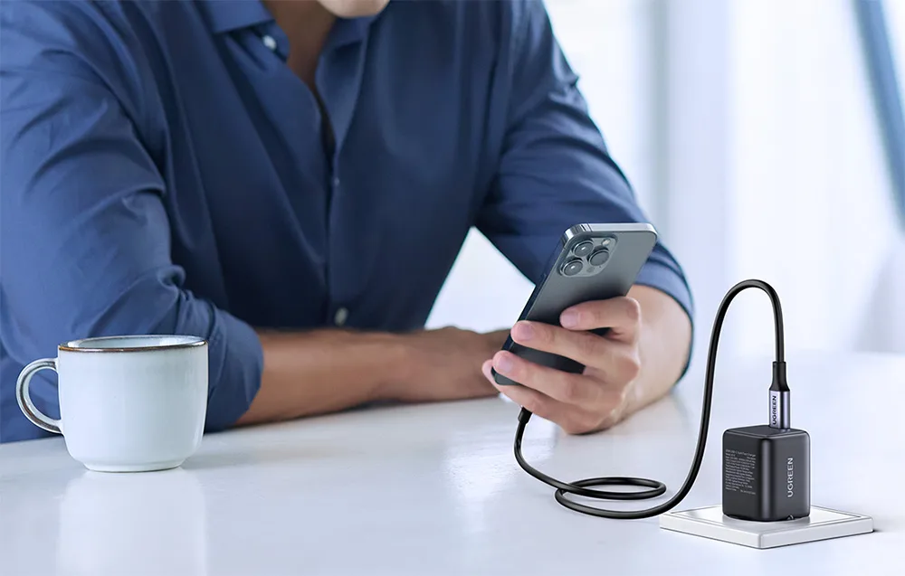 Person using a smartphone while charging it with the UGREEN X513 charger next to a cup of coffee