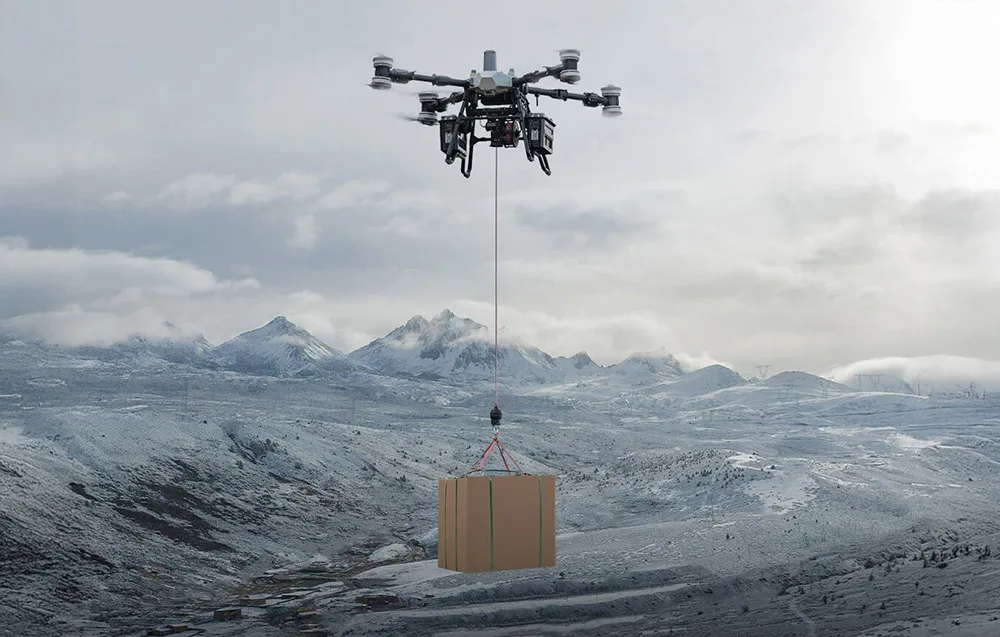 Dron transportowy lecący nad ośnieżonymi szczytami górskimi, niosący na lince duże tekturowe pudło