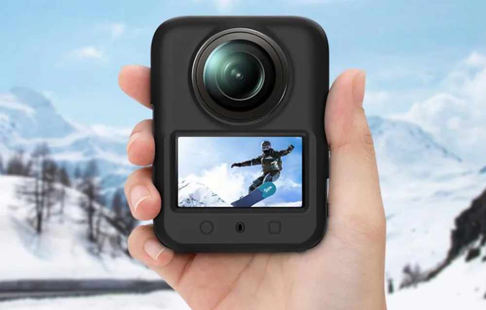 Dłonie trzymające czarną kamerę 360 stopni z obrazem snowboardzisty na ekranie na tle gór