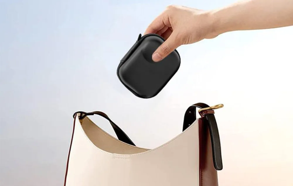Hand holding a black mini camera case above a beige handbag