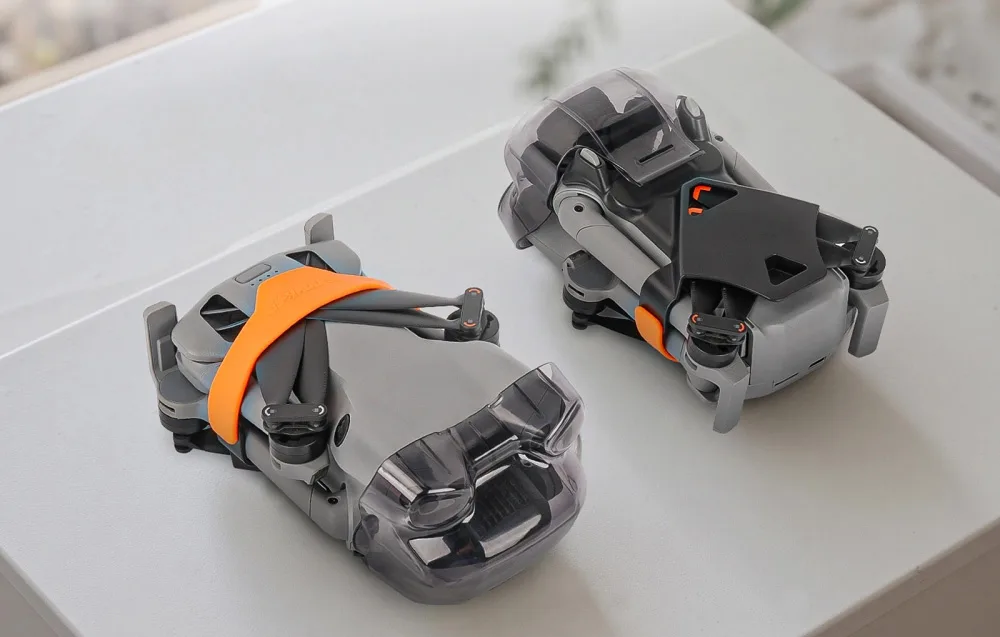 Two folded drones with different gimbal protectors, including a DJI Mini 5 Pro with Sunnylife protector and orange strap