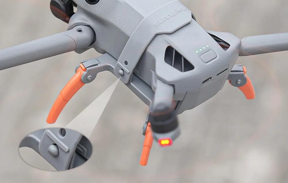Widok z góry na tylną część drona DJI Mini 5 Pro z zamontowanymi pomarańczowymi nóżkami oraz powiększeniem zbliżenia mechanizmu mocującego