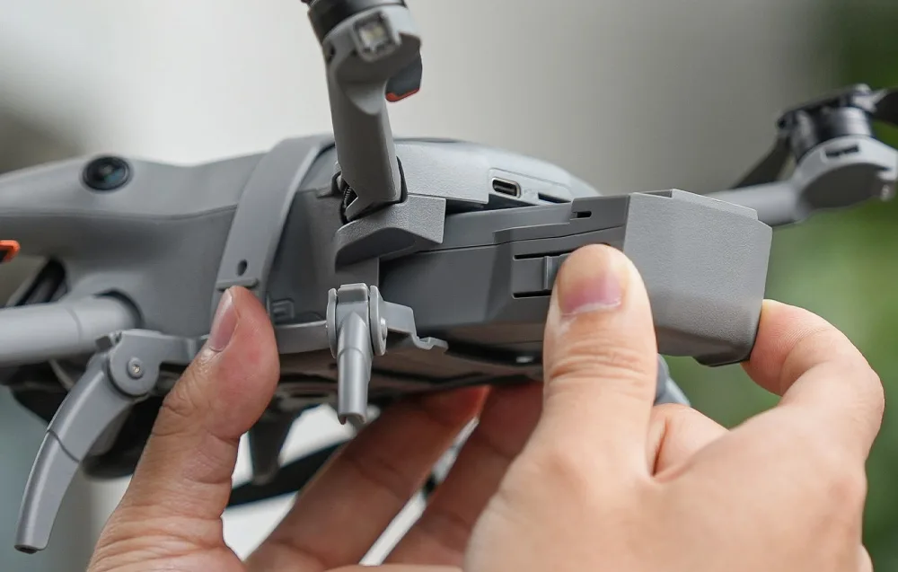 Zbliżenie na ręce wyjmujące lub wkładające akumulator do drona DJI Mini 5 Pro