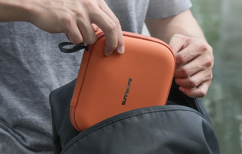 Person placing the orange Sunnylife case into a backpack