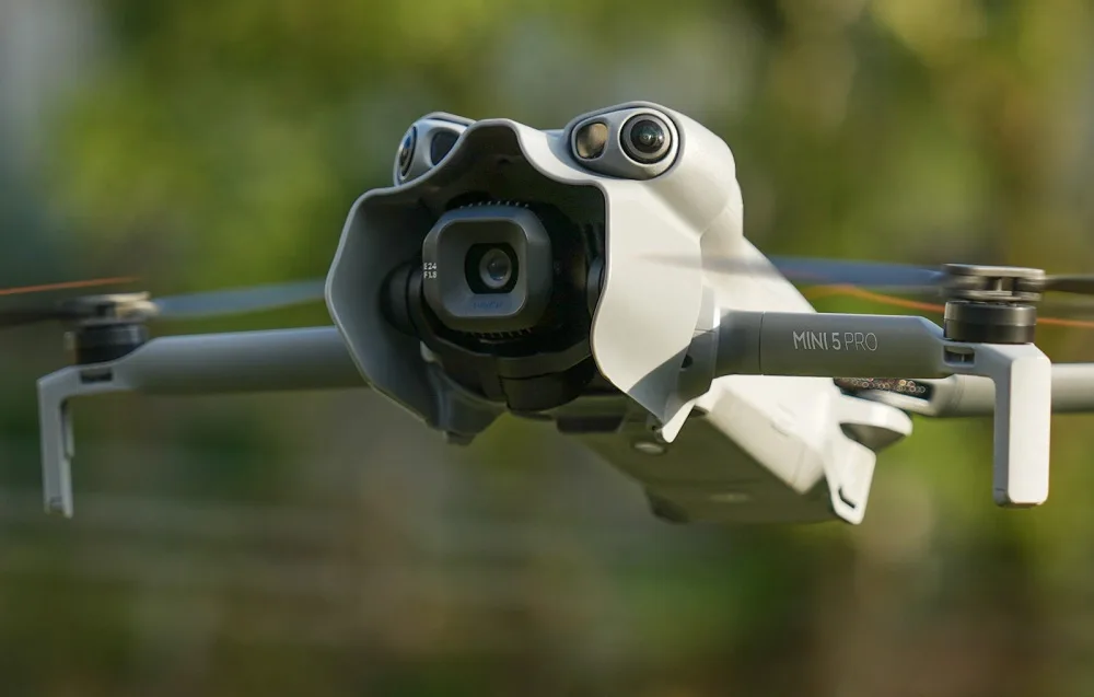 DJI Mini 5 Pro drone in flight with a light gray aerodynamic camera sun hood