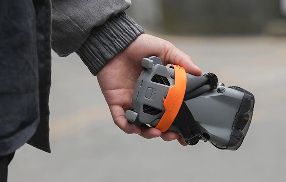 Osoba trzymająca złożonego drona DJI Mini z założoną pomarańczową opaską mocującą śmigła