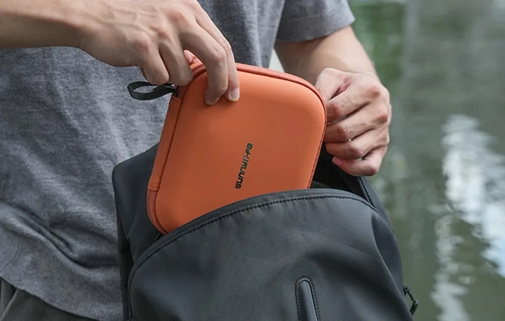 Ręce wkładające pomarańczowe etui Sunnylife do szarego plecaka