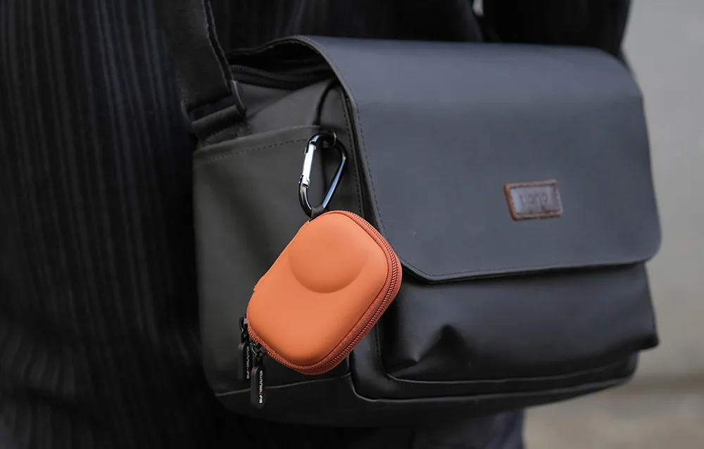Sunnylife orange camera case clipped to a black shoulder bag with carabiner