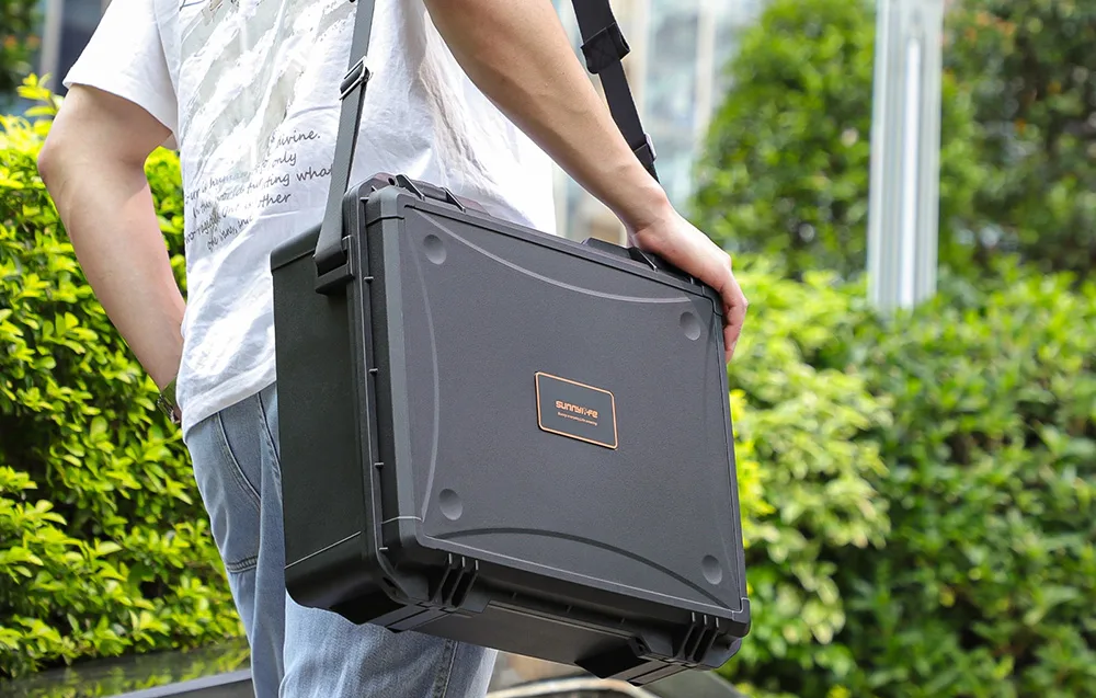 Person carrying a large Sunnylife protective case with a shoulder strap outdoors in a green setting