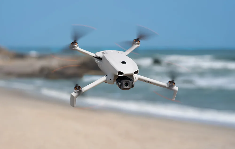 White drone flying above a blurred beach and ocean background viewed from above