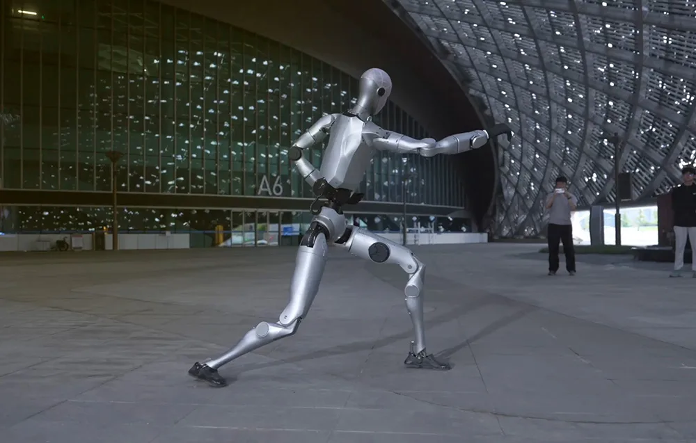 UNITREE H2 Edu humanoid robot performing a dynamic martial-arts-inspired move in front of a modern building