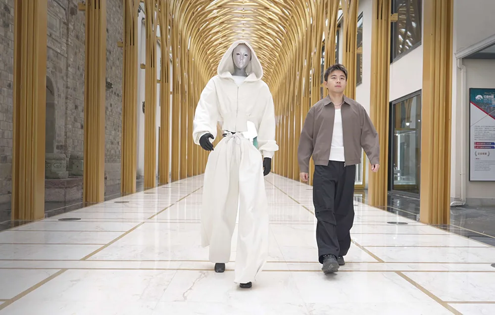 UNITREE H2 humanoid robot walking down a corridor next to a man