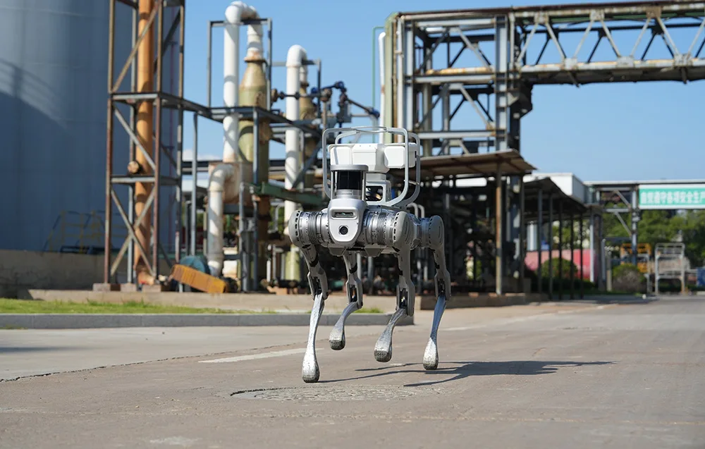 UNITREE B2 quadruped robot walking on a road in an industrial area with pipes and metal structures in the background