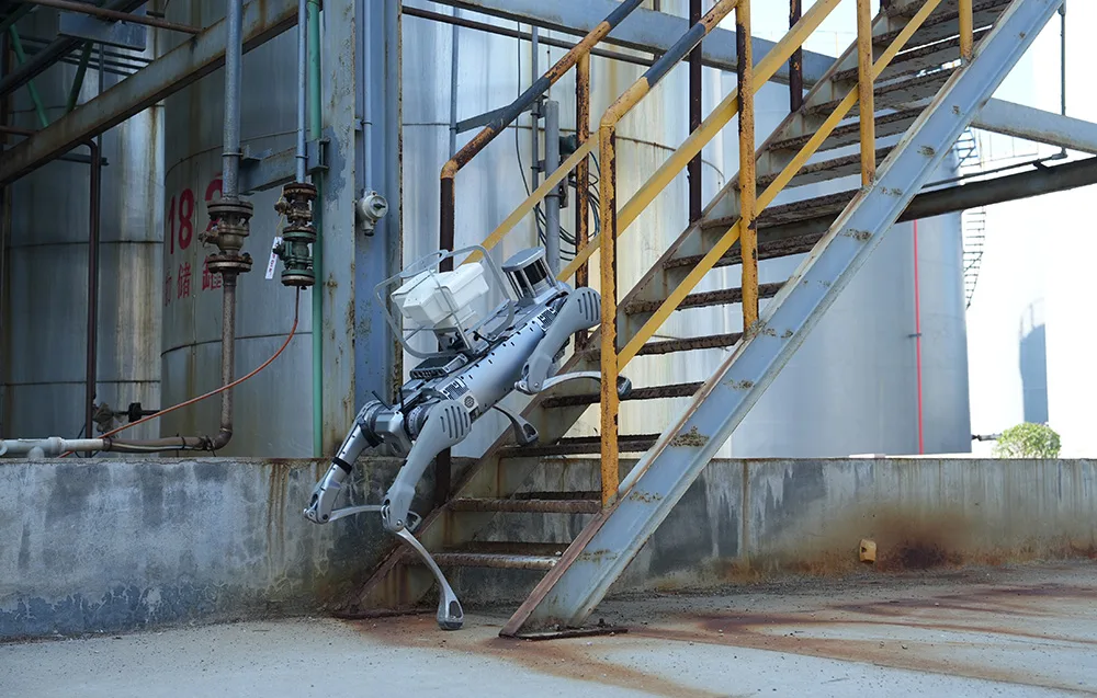 UNITREE B2 quadruped robot climbing rusty metal stairs at an industrial site