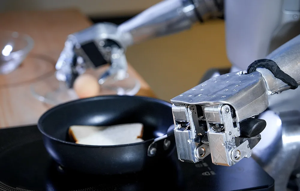 Robotyczne ramię trzyma patelnię z kromką chleba na kuchence indukcyjnej