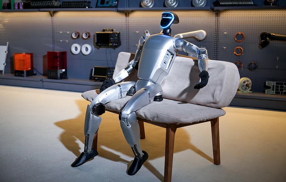 Humanoidalny robot marki Unitree siedzi na kanapie w pomieszczeniu z narzędziami