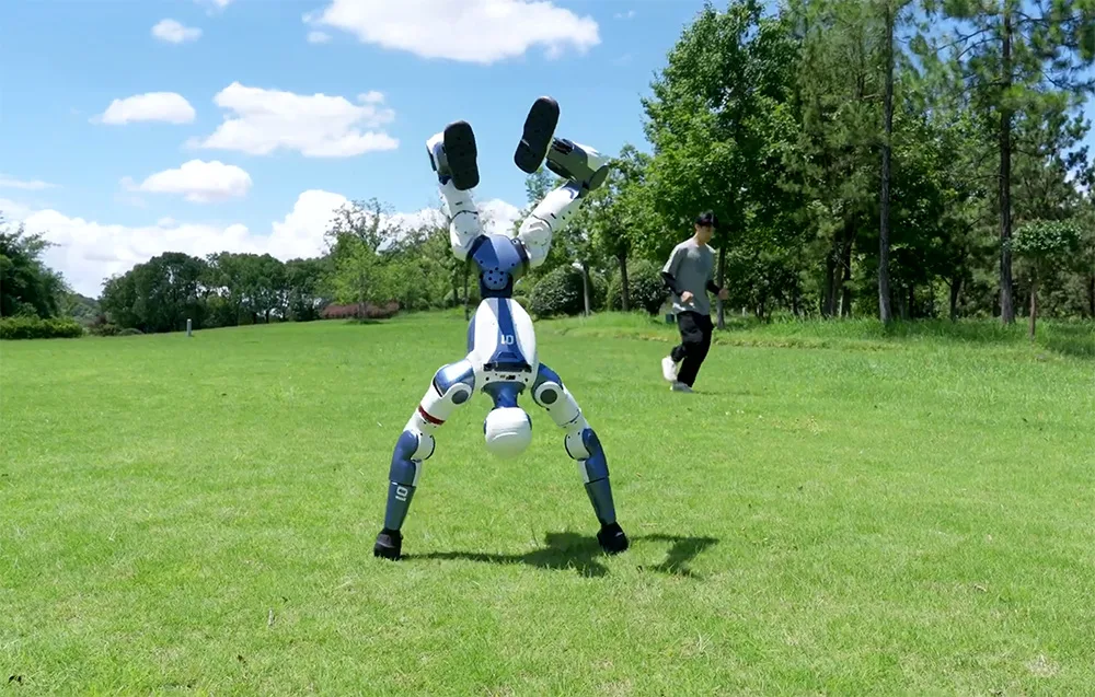 UNITREE R1 Edu U2 humanoid robot balancing on its hands on grass next to a running person