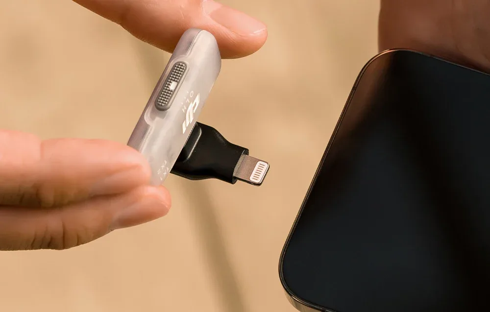 Hands holding a white DJI receiver with a black Lightning adapter connected at the edge of a smartphone