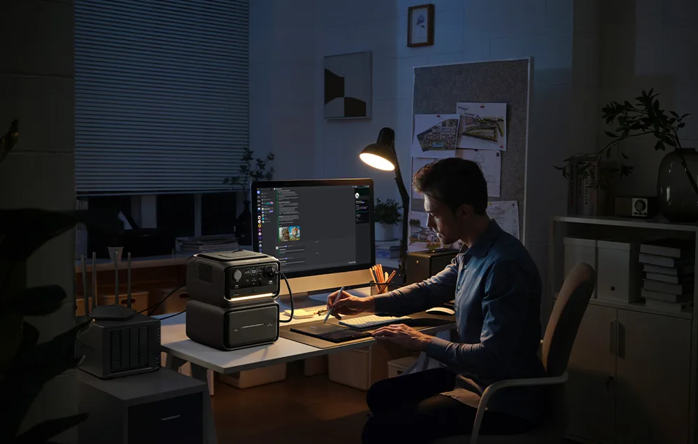 Mężczyzna pracuje wieczorem przy biurku, na którym pali się lampa i leży stacja zasilania