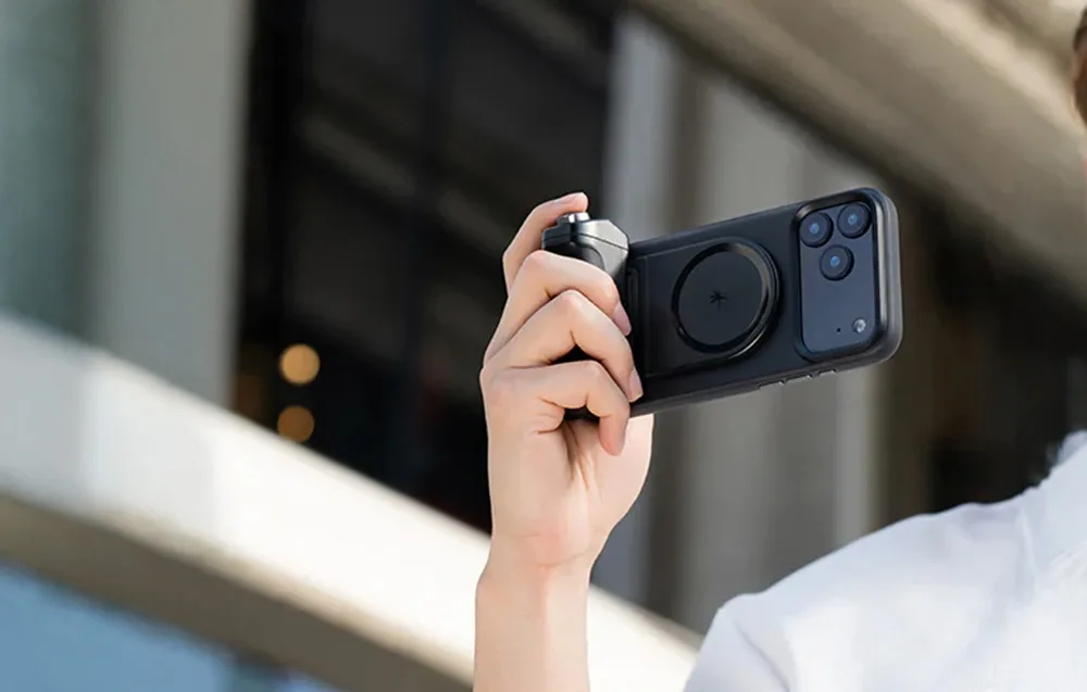 Hand holding a smartphone with the black PGYTech MagCam 2 grip while taking photos outdoors