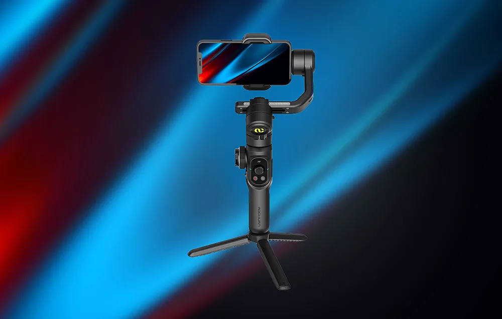 Czarny gimbal ze smartfonem w poziomie ustawiony na mini statywie na granatowo-niebieskim tle.