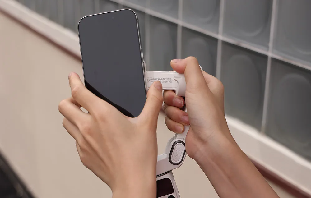 Ręce mocują smartfon do uchwytu magnetycznego na gimbalu.