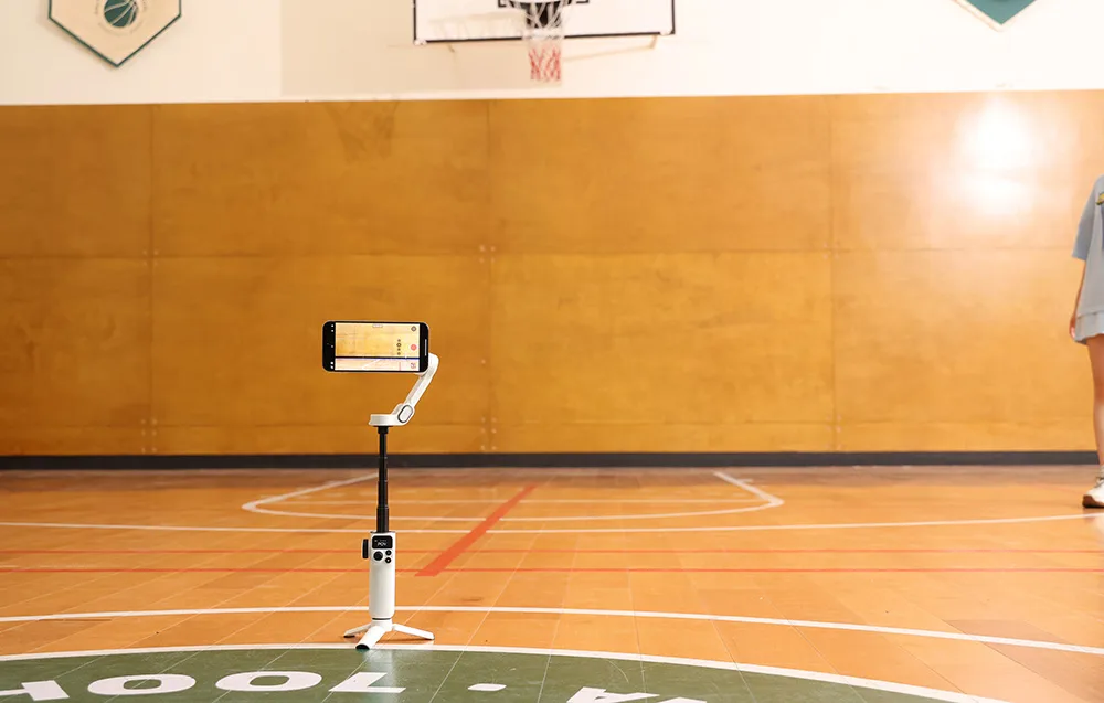 Gimbal ze smartfonem ustawiony na statywie na hali sportowej podczas nagrywania.
