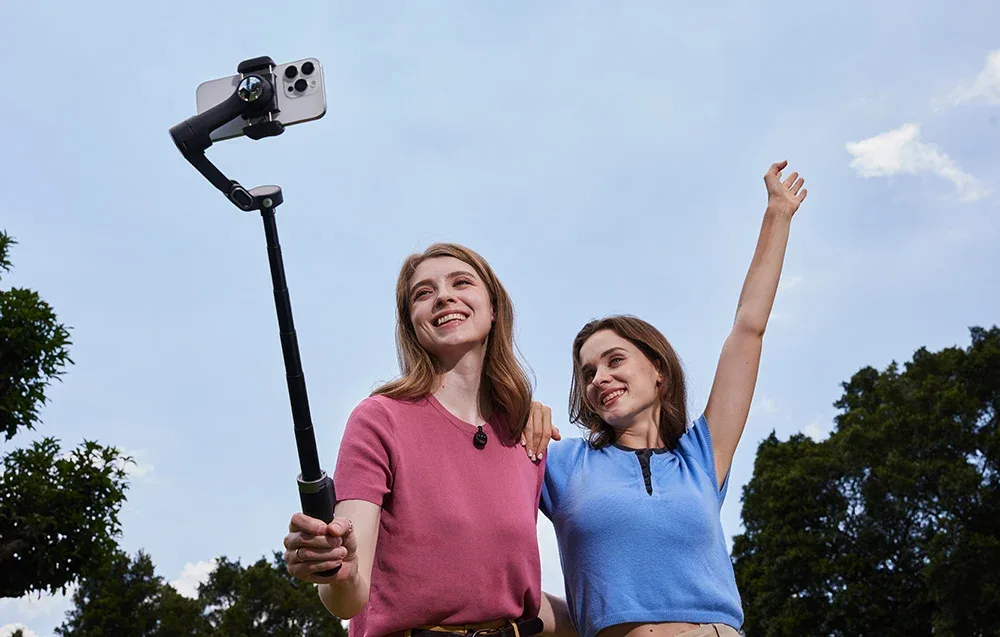 Dwie kobiety robią wspólne selfie na świeżym powietrzu, używając gimbala z wysięgnikiem.