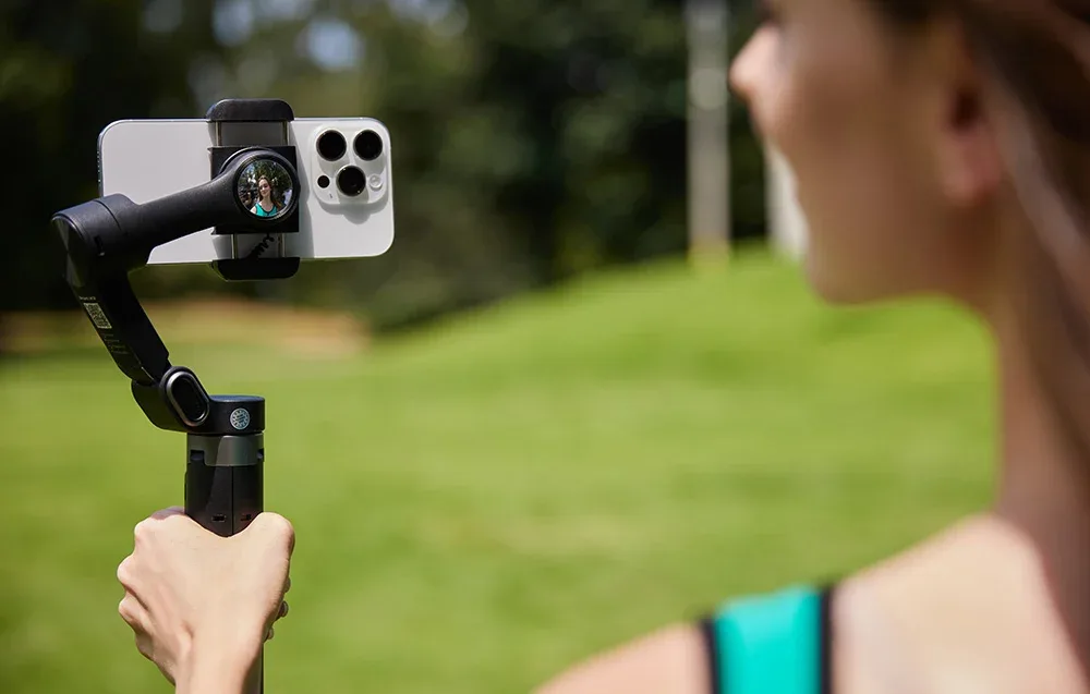 Kobieta filmuje się na zewnątrz, trzymając gimbal ze smartfonem podczas nagrywania.