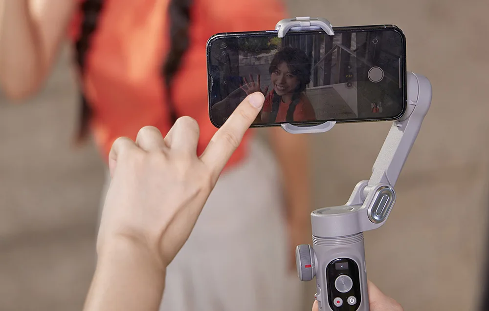 Smartfon na gimbalu nagrywa selfie, a użytkownik dotyka ekranu, ustawiając ostrość.
