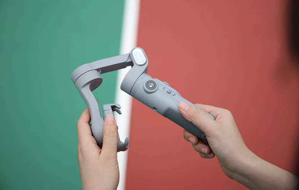 Ręce rozkładają gimbal, przygotowując urządzenie do użycia na tle boiska