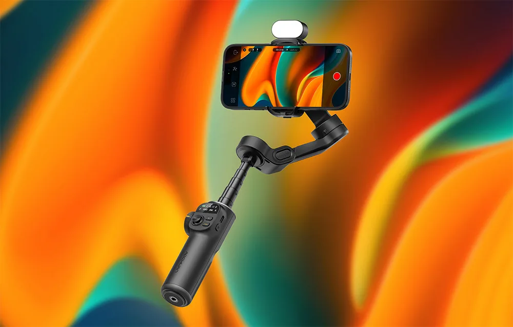 Czarny gimbal ze smartfonem i wbudowaną lampą na kolorowym gradientowym tle w odcieniach pomarańczu i zieleni.