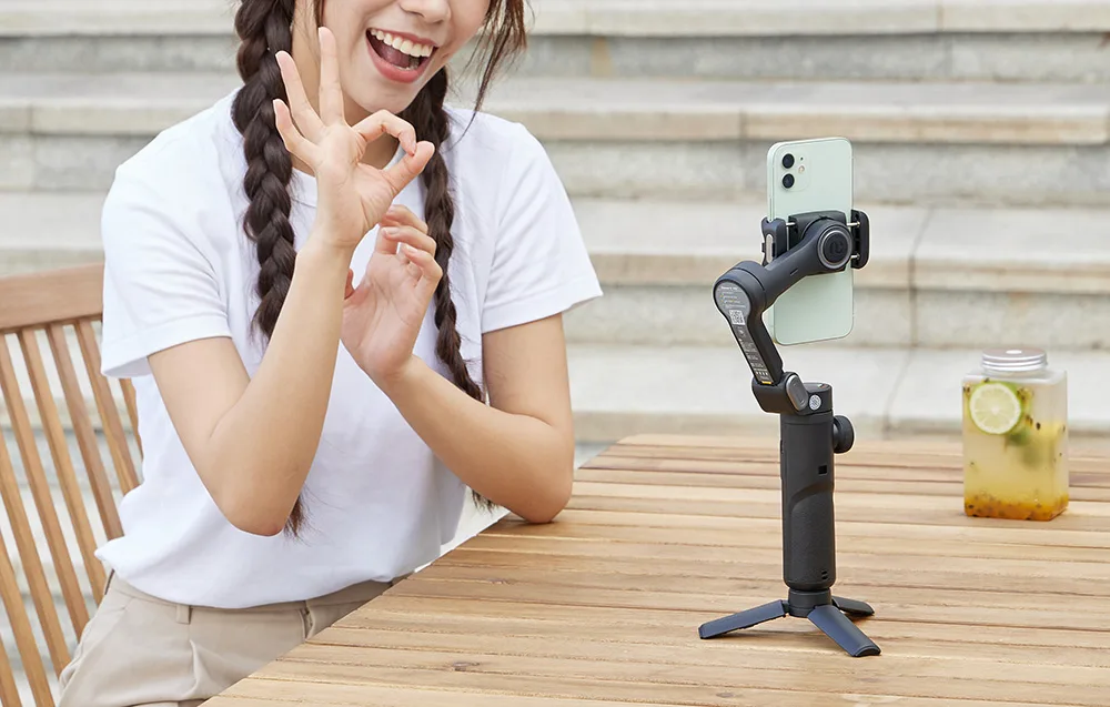 Woman recording a video with a smartphone mounted on the AOCHUAN XE gimbal while making an OK gesture
