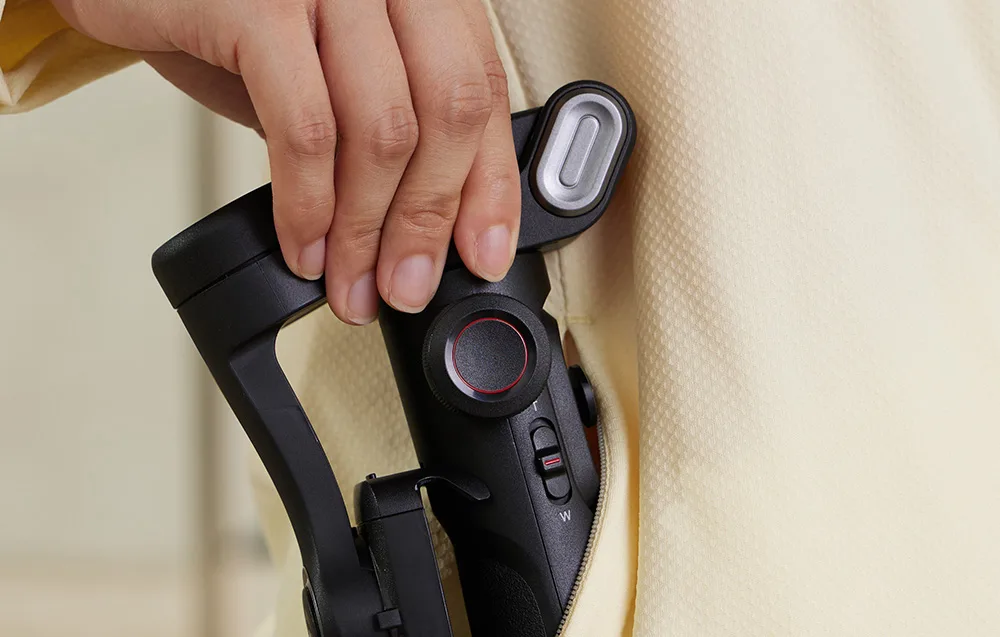 Hand placing the folded AOCHUAN XE gimbal into a hoodie pocket