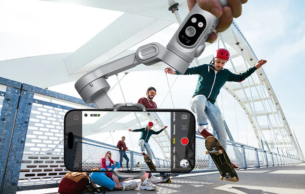 Dłoń trzymająca gimbal od dołu, nagrywający grupę skateboardzistów na moście.