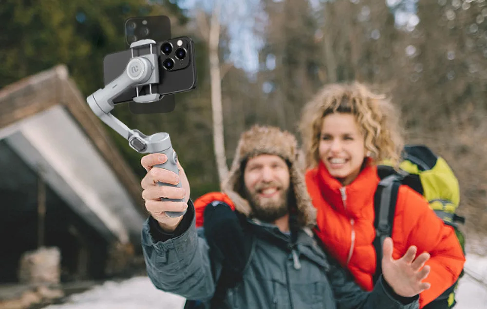 Para turystów w zimowym lesie robi selfie gimbalem ze smartfonem.