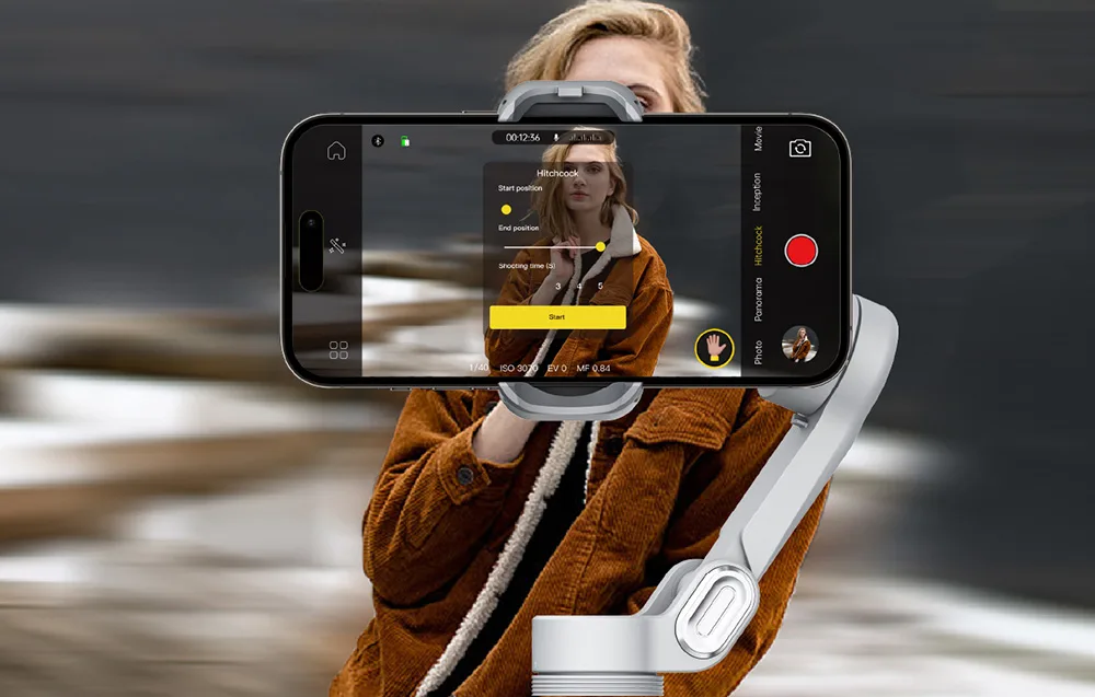 Gimbal ze smartfonem pokazujący interfejs podczas filmowania kobiety w brązowej kurtce.