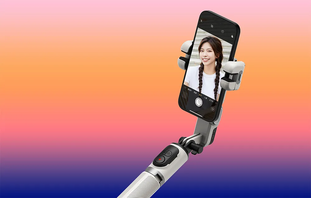 Gimbal na wysięgniku ze smartfonem wyświetlającym selfie uśmiechniętej kobiety na pomarańczowym tle.
