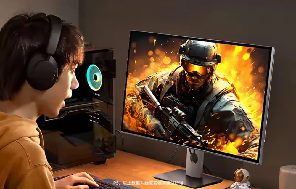 Gracz w słuchawkach przy monitorze pokazującym scenę z gry FPS z żołnierzem i wybuchami w tle