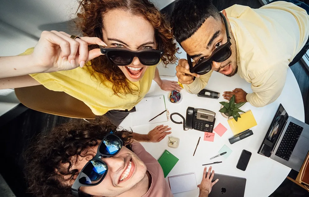 Three people wearing VITURE XR Beast glasses gather around a table with laptops and phones.