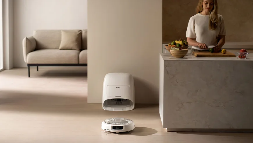 DJI Romo robot vacuum and its docking station in a kitchen near a woman preparing fruit