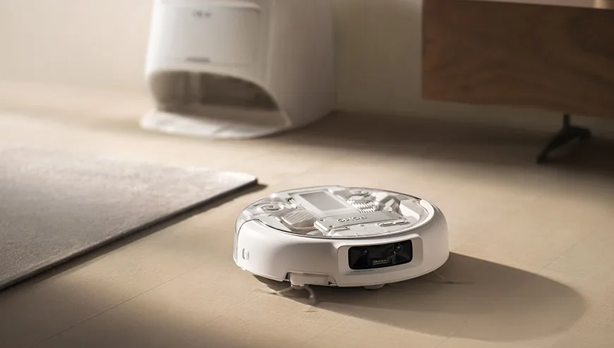DJI Romo robot vacuum moving across a light-colored floor near the docking station